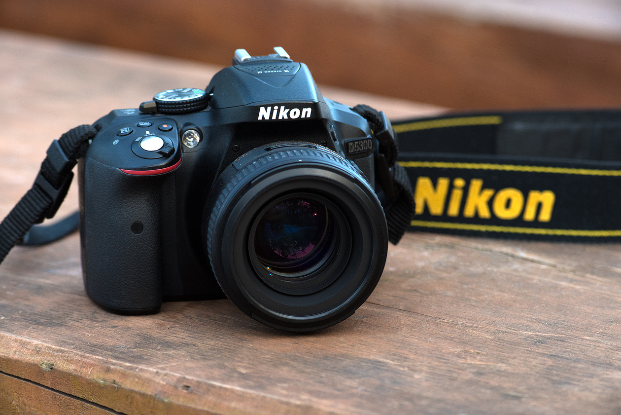 Nikon DSLR with a fast prime lens on a wooden table, its strap with the Nikon logo beside it